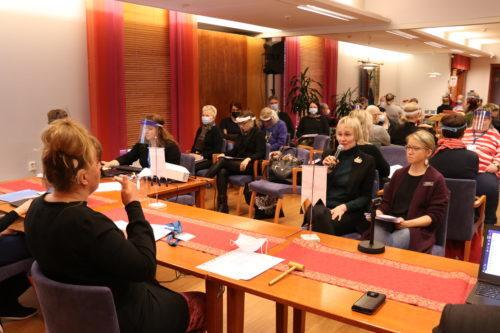 Vuosikokouksen puheenjohtaja ja osallistujia. Puheenjohtajaa tulkkaa tulkki.