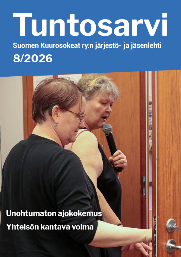 Riitta Lahtinen opastaa Sanna Nuutista ovelle. Riitta pitää kädessään mikrofonia ja puhuu. Sanna pitää kädellään ovenkahvasta. Sannalla on lyhyet ruskeat hiukset ja silmälasit. Hänellä on tumma paita. Riitalla on lyhythihainen tumma asu.